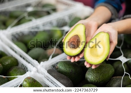 Close-up of two halves of ripe hass avocado in hands of female fruit sorting factory worker.. Royalty-Free Stock Photo #2247363729