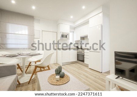 Studio apartment with an open plan kitchen with white cabinets and a round white dining table with resin chairs Royalty-Free Stock Photo #2247371611