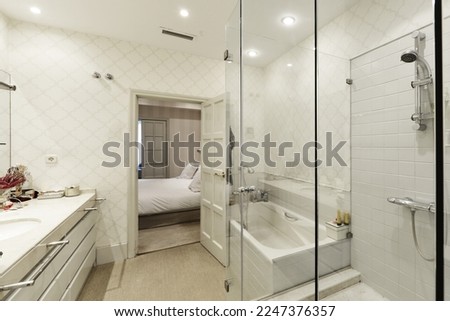 Bathroom with wall covered with white mosaic tile, two-bowl white marble sink with drawers and separate bathtub and shower cabin with glass door and partitions Royalty-Free Stock Photo #2247376357