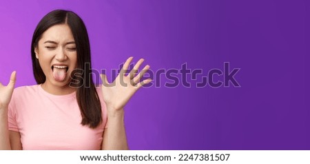 Close-up silly moody asian girl complaining act immature and bothered, raise hands unsatisfied show tongue aversion disgust, close eyes, react terrible disgusting thing, stand purple background. Royalty-Free Stock Photo #2247381507