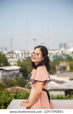 Portrait picture an Asian woman in a pink dress, she is looking at a camera with high view urban background.