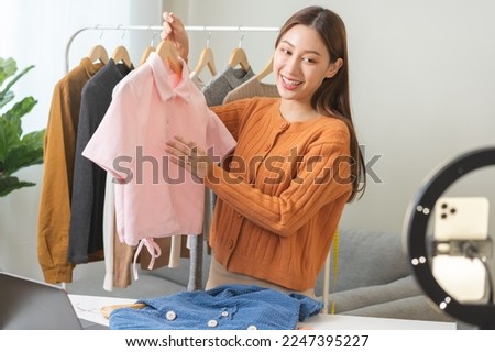 Vlogger, blogger small SME business asian beautiful woman using mobile phone video call for sell clothes live stream selling online, show product present detail at home office, entrepreneur ecommerce