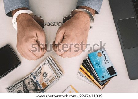 Hands of a fraudster with handcuffs on a background of us dollars and credit cards. Fraud, cyber crime concept. credit card fraud. Arrest of an entrepreneur in the workplace. Royalty-Free Stock Photo #2247431339