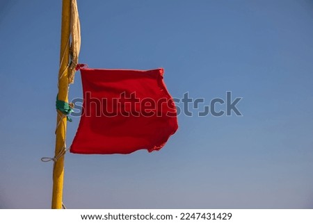 The red flag flutters in the wind. Blue sky. Strong wind. Swimming is prohibited.
