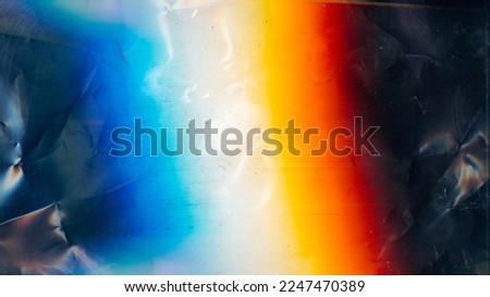 Distressed overlay. Dust scratches texture. Creased old film noise. Orange blue white rainbow color glow on dark wrinkled uneven abstract background.