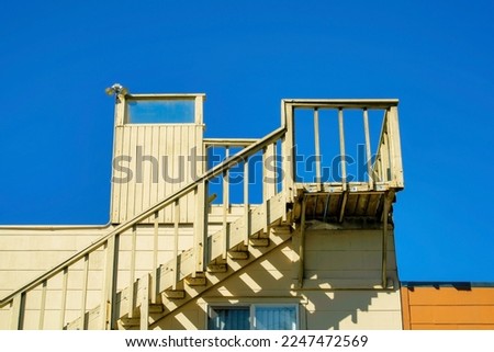 Stairs leading to the roof of the house to a flat patio with beige or yellow paint with blue dark sky in the late afternoon sun and shade. In a suburban area of the neighborhood roof access on top.