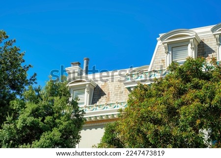 Weathered or aged structure with faded roof tiles and visible decorative facade exterior with front yard trees and blue clear sky. Copy space blue sky in the abandoned building in neighborhood.