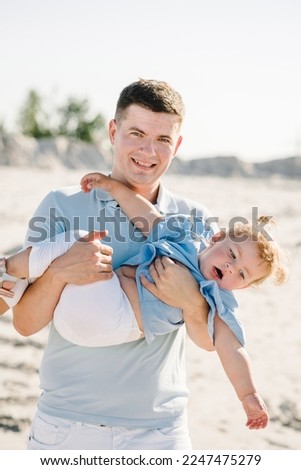 Father and daughter. Dad hugs little kid walking on the sandy beach. Father's day. Family and childhood concept. Portrait of a happy child girl with daddy playing on the sand together outdoors.