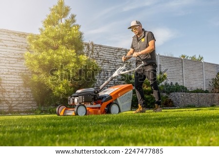 Man mowing lawn in the backyard of his house. Man with lawn mower. Royalty-Free Stock Photo #2247477885