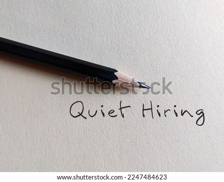 Pencil writing on beige background with handwritten text QUIET HIRING - HR buzz word of recruiting strategy, stand out employees who going above and beyond get more attention, money and praise 
