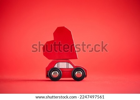 Red model of car delivering red paper heart on red background. February 14 card for holiday concept. Creative greeting card for Saint Valentine day.