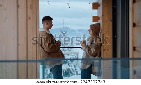 Portrait of beautiful 20s young Caucasian couple enjoying the view of snowy mountains while having a morning coffee