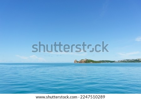 A photo of a rocky, isolated outcrop stretching out into the sea. The picture was taken from a ferry crossing the calm waters from Ko Samui to Ko Phangan in Thailand. 