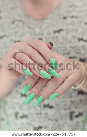 Female hand with long nails and neon light green manicure with bottles of nail polish