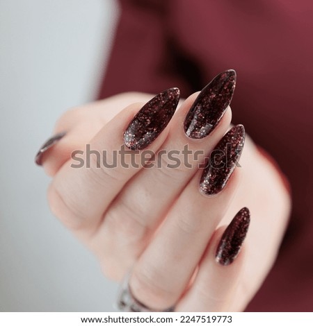 Woman hand with long nails and a bottle of dark red burgundy nail polish