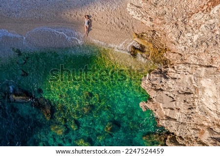 A fashionable girl is resting alone on an empty beach, washed by a wave next to the rocks. Drone shot top view. High quality photo