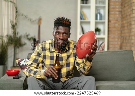 Young African man watching sport match on television and supporting his favorite team. Happy man enjoying victory, watching sports competition on tv.