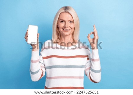 Photo of pretty charming lady wear striped pullover showing okey gadget empty space isolated blue color background