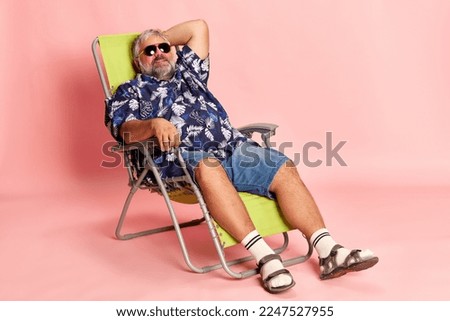 Portrait of mature man in stylish shirt and sunglasses lying, posing over pink studio background. Relaxation, vacation. Concept of american style, culture, emotions, facial expression, lifestyle