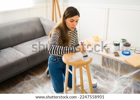 Beautiful young woman painting a stool on her DIY home improvement project or furniture flipping