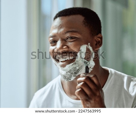 Face, shaving and razor with a black man grooming in the bathroom mirror of his home for beauty or skincare. Beard, shave and blade with a handsome male in the morning for his hair removal routine Royalty-Free Stock Photo #2247563995