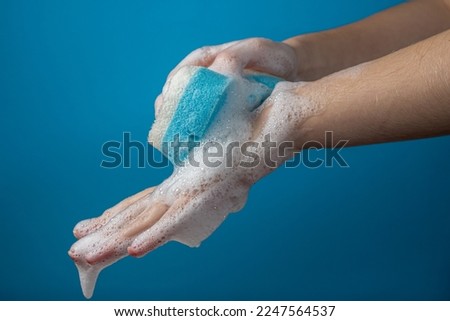 Women's hands in soapy foam on a blue background. Hand washing and hygiene concept.