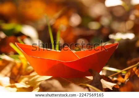 Orange paper boat on the background of autumn leaves.