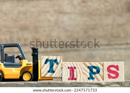 Toy yellow forklift hold letter block t to complete word tips on wood background