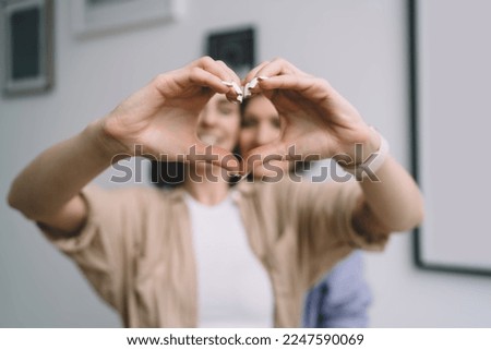 Soft focus of anonymous female in casual wear with wristwatch showing heart sign sending love energy while mother standing behind