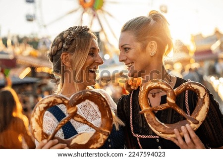girlfriends look at each other  holding pretzel or brezen on a Bavarian fair or oktoberfest or duld in national costume or Dirndl in germany  Royalty-Free Stock Photo #2247594023