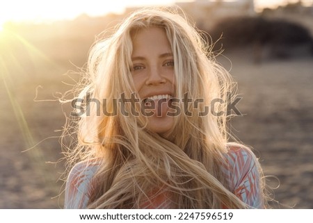 Pretty female blond model is at the beach enjoying the sunset light. She smiles and looks happy.
