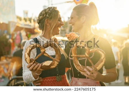 Two girlfriends together holding pretzel or brezen on a Bavarian fair or oktoberfest or duld in national costume or Dirndl in germany  Royalty-Free Stock Photo #2247605175