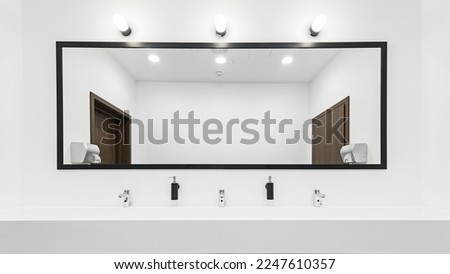 Modern toilet with a large illuminated mirror. Wide sink with taps for several people. Bright and spacious bathroom. Royalty-Free Stock Photo #2247610357