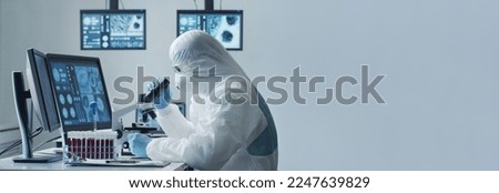 Scientist in protection suit and masks working in research lab using laboratory equipment: microscopes, test tubes. Coronavirus 2019-ncov hazard, pharmaceutical discovery, bacteriology and virology. Royalty-Free Stock Photo #2247639829