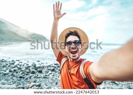 Happy handsome man taking selfie picture with smart mobile phone device outside - Travel blogger on live streaming in social platform - Tourism, travel, people and technology concept