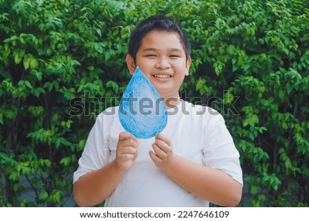 Cute asian boy holding paper cut water drop on green background. World water day. Save water concept. 