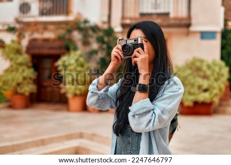 Portrait of asian female tourist or student walking and making photos on retro camera on city streets. Vacation and tourism concept.