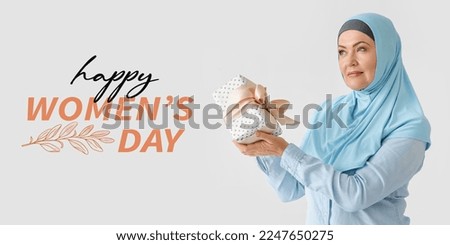 Beautiful mature Muslim woman with gift box on light background. Greeting card for Women's Day