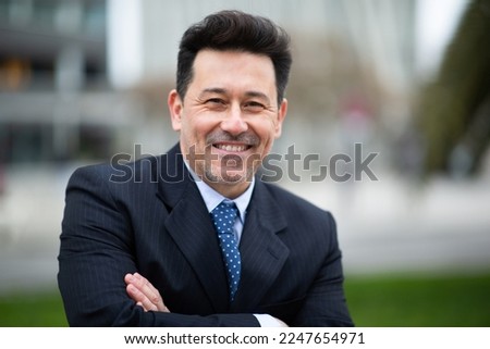 Close up portrait of smiling mature businessman standing outside with his arms crossed
