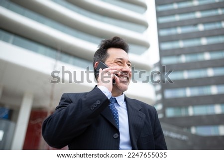 Close-up portrait of happy mature businessman standing against a building making a phone call
