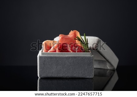 Prosciutto with rosemary in a gray gift box on a black background. Concept of the theme of expensive food. Royalty-Free Stock Photo #2247657715