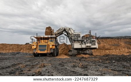Large quarry dump truck and excavator. Big mining truck work coal deposit. Loading coal into body truck. Production useful minerals. Mining mining machinery to transport coal from open-pit production Royalty-Free Stock Photo #2247687329