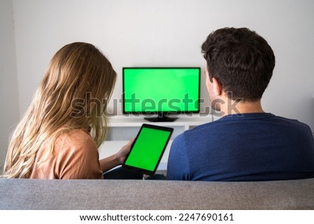 Young couple is sitting on the couch at home with a tablet. Green screen, blank space for insertion. Online shopping.