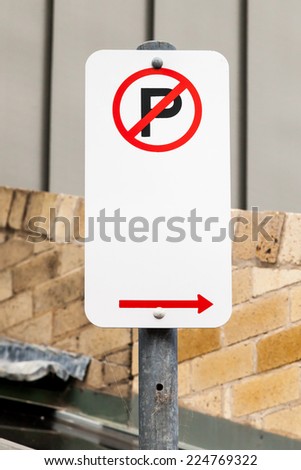 Red, white and black NO PARKING sign with red arrow pointing right against urban buildings on a city street