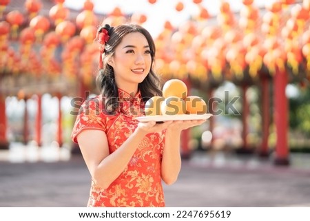 Happy Chinese new year. Beautiful asian woman wearing traditional cheongsam qipao dress holding fresh oranges in Chinese Buddhist temple. Emotion smile