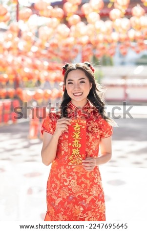 Vertical picture. Happy Chinese new year. A young lady wearing traditional cheongsam qipao dress holding blessing fortune card in Chinese Buddhist temple. Chinese text means blessed by a lucky star. 