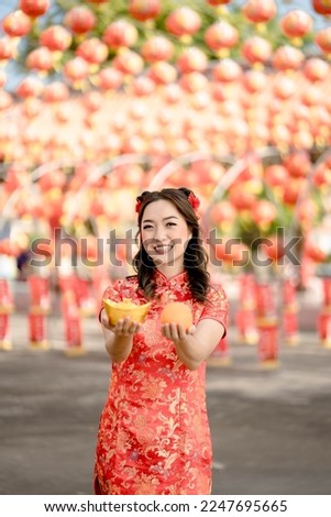 Vertical picture. Happy Chinese new year. A young lady wearing traditional cheongsam qipao dress holding ancient gold money and orange fresh in Chinese Buddhist temple. Celebrate Chinese new year