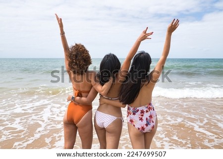 Attractive mature woman next to two young, pretty, brunette South American women in bikinis taking funny photos of each other with their backs turned. Concept vacation, girlfriends, summer.