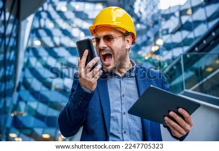 Something is wrong on building site. Angry construction engineer yelling on head of the construction site while talking with him via mobile phone. Construction concept Royalty-Free Stock Photo #2247705323