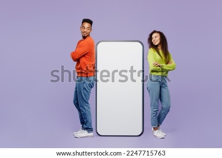 Full body sideways young couple two friends family man woman wear casual clothes together stand near big huge blank screen mobile cell phone with area isolated on pastel plain light purple background